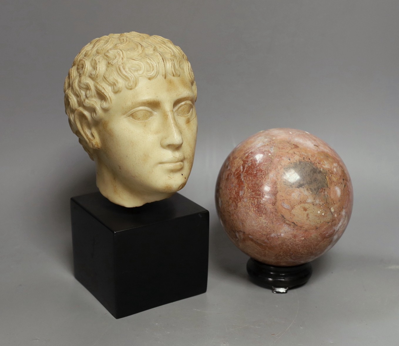 A simulated marble Roman head ornament, 24 cm and a rouge marble ball on stand, 15 cm